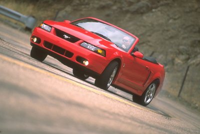 2003 Ford Mustang - A red 2003 Ford Mustang convertible is captured in motion on a winding road.