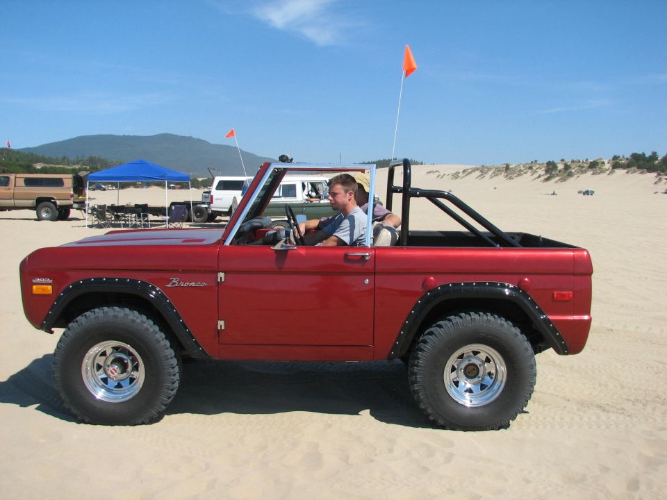 Red open-top early Ford Bronco with driver on a sand dune