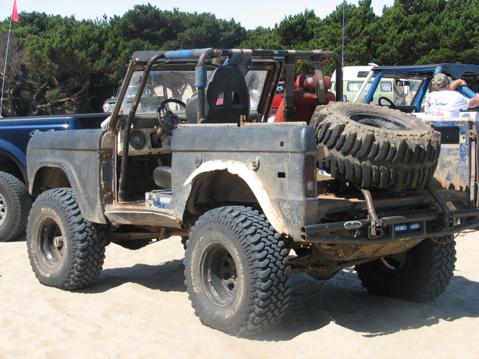 Bare-metal lifted early Bronco with spare tire on rear, rear three-quarter view