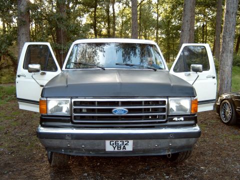1989 Ford Bronco - White Ford F-Series truck parked outdoors with its doors open, showing the front grille and headlights.