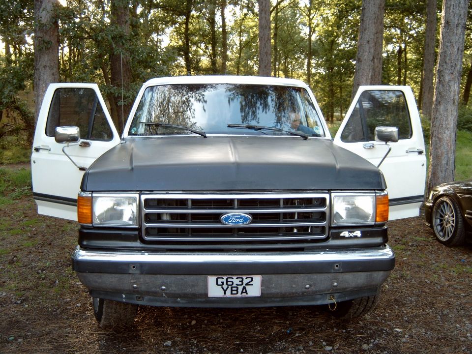 Front view of a white Ford F-Series truck with doors open, black hood, and a license plate reading G632 YBA. Another vehicle is partially visible on the right