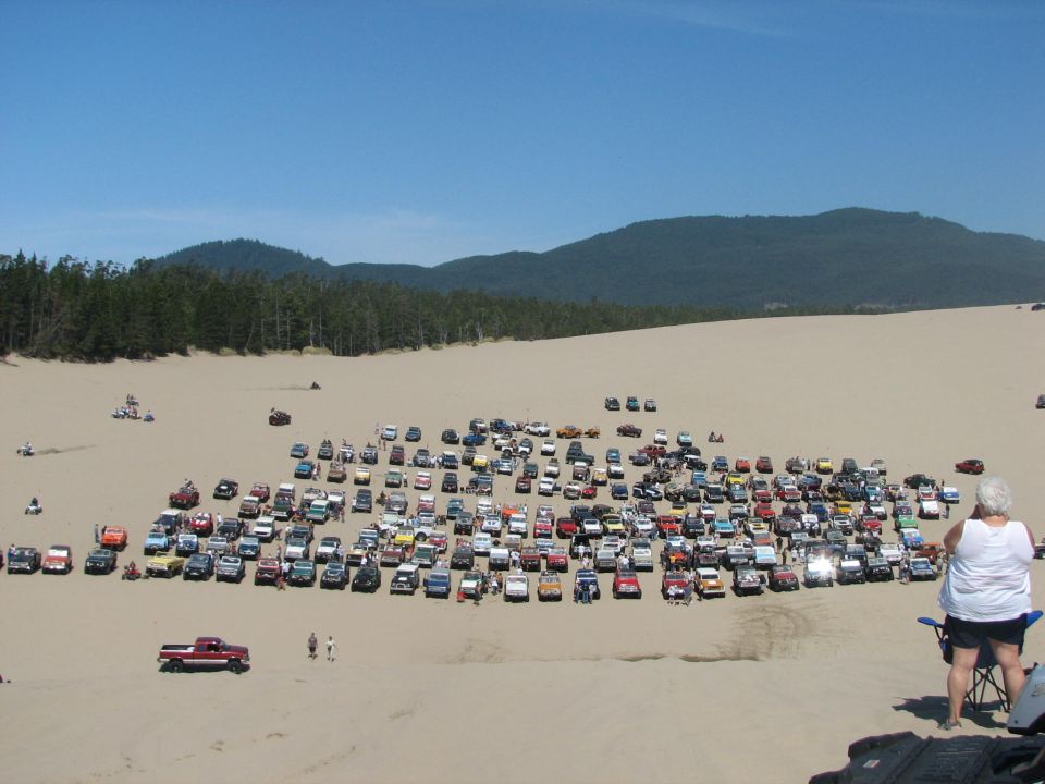 Crowd of off-road vehicles on a dune with a seated woman watching