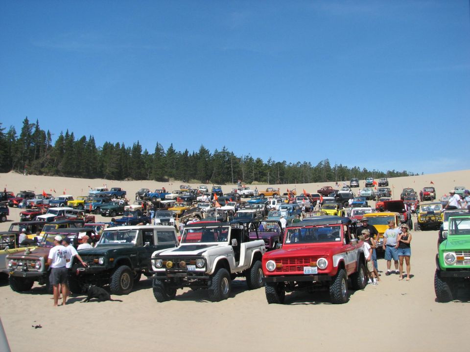 Row of early Broncos and 4x4s lined up on sand under blue sky