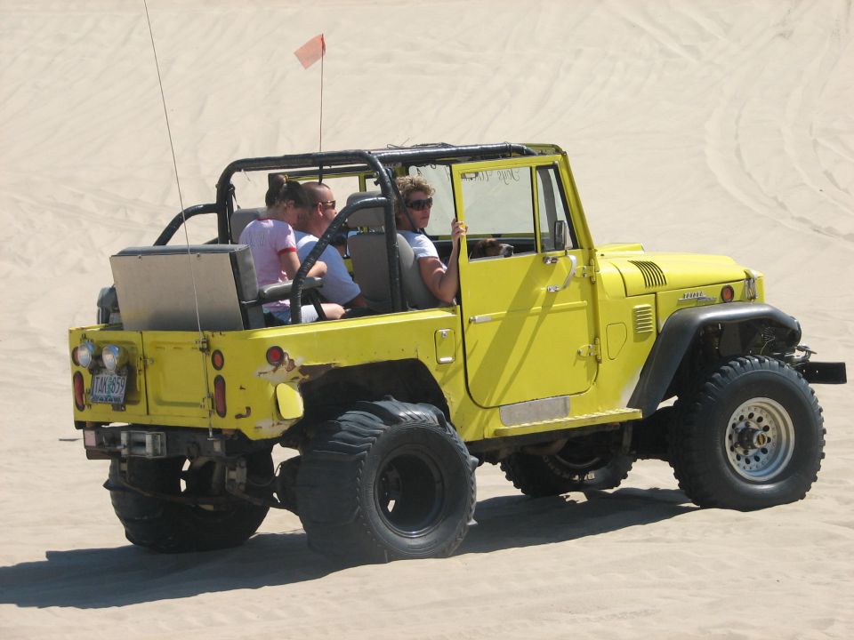 Yellow open-top 4x4 carrying passengers across the sand
