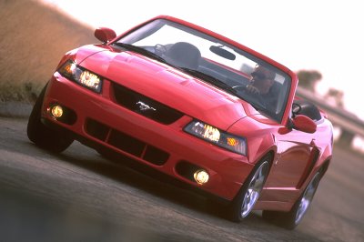 2003 Ford Mustang - A red 2003 Ford Mustang convertible is captured in a dynamic shot from the front three-quarter angle.