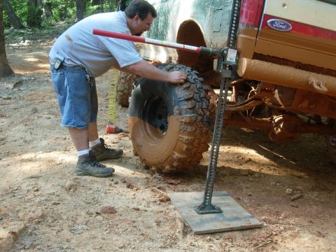 1990 Ford Bronco - A man uses a Hi-Lift jack to lift a muddy Ford Bronco on a dirt path.