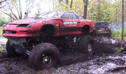 1978 Ford Bronco - A heavily modified red car with oversized tires navigates a muddy off-road course, with another vehicle visible in the background.