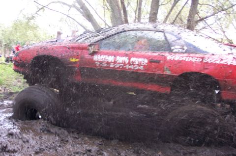 1978 Ford Bronco - Muddy red car with text on door stuck in a mire, tires barely visible.