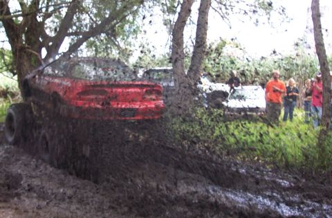1978 Ford Bronco - A red SUV is deeply mired in mud, with several people observing the scene.