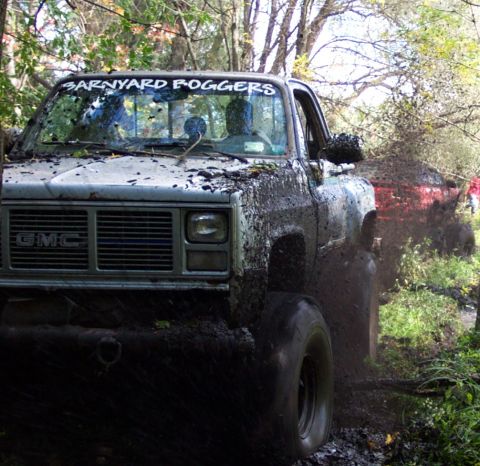 1978 Ford Bronco - Muddy GMC truck navigates a challenging off-road course, with another vehicle in the background.