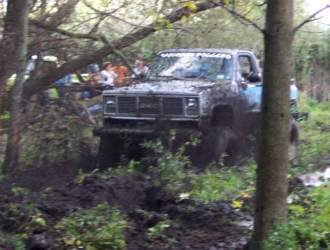 1978 Ford Bronco - A GMC pickup truck navigates a muddy off-road course, its front grille clearly visible.