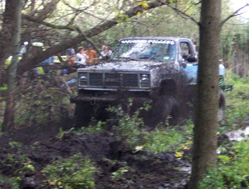 Mud-covered GMC pickup truck, front view, with "WARPED POLLERS" text on windshield