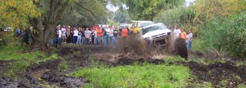 1978 Ford Bronco - Several off-road vehicles navigate a muddy track with a crowd of onlookers.