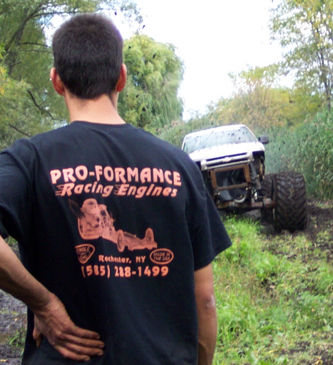 White off-road vehicle with large tires stuck in mud, front end removed