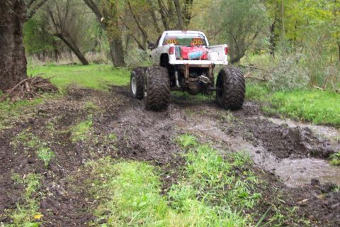 1978 Ford Bronco - A modified white truck with oversized tires navigates a muddy, wooded trail.