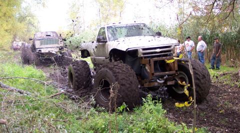 1978 Ford Bronco - Off-road vehicles navigate a muddy trail, kicking up dirt as they go.