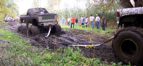 1978 Ford Bronco - A group of people watch as a heavily modified pickup truck struggles in a muddy off-road course.