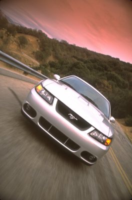 2003 Ford Mustang - A silver 2003 Ford Mustang drives down a scenic road under a dramatic sky.