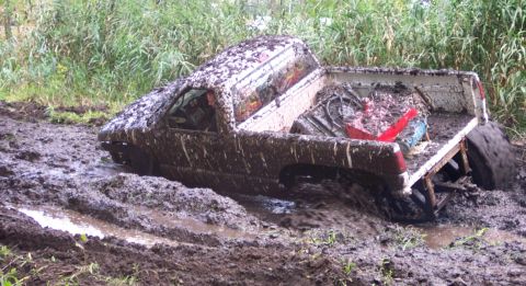 1978 Ford Bronco - A pickup truck is stuck deep in the mud, with its rear wheel spinning.