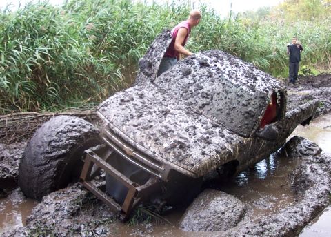 1978 Ford Bronco - A truck is deeply stuck in mud and water, with two individuals observing the scene.
