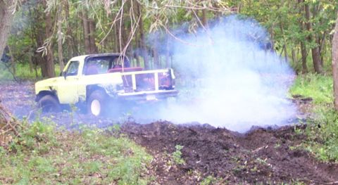 1978 Ford Bronco - A yellow pickup truck is stuck in the mud, kicking up a large cloud of white smoke.