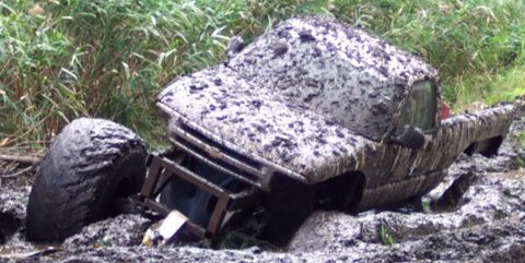 1978 Ford Bronco - This truck is heavily covered in mud and appears to be stuck in a ditch, with only its tires and part of the body visible.