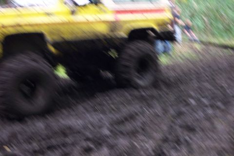 1978 Ford Bronco - A yellow off-road vehicle navigates a muddy terrain, with two people visible in the background.