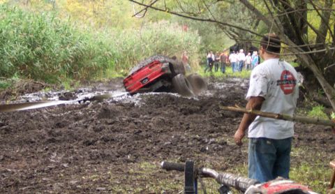 1978 Ford Bronco - A red SUV is deeply stuck in a muddy, off-road environment with onlookers observing the scene.