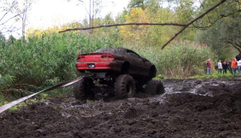 1978 Ford Bronco - Modified red Chevrolet Camaro is stuck deep in the mud during an off-road event.
