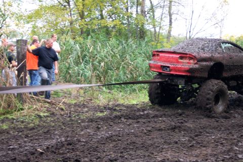 1978 Ford Bronco - A heavily muddied car is being pulled out of a bog by a rope, with onlookers observing the scene.