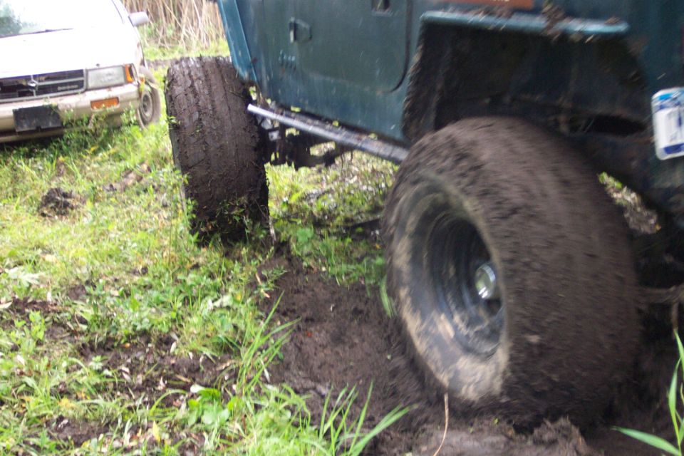 Green off-road vehicle stuck in mud, with a white SUV in the background