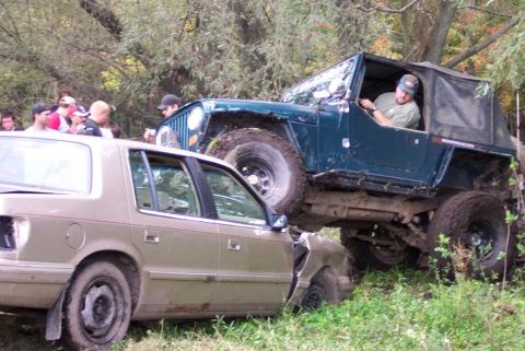 1978 Ford Bronco - A Jeep Wrangler is driven on top of a sedan during an off-road event.