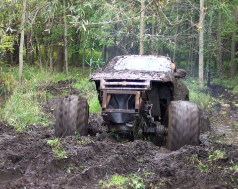 1978 Ford Bronco - A heavily mud-covered SUV is stuck in a muddy forest path, its tires deep in the mire.
