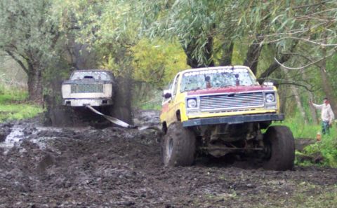 1978 Ford Bronco - Two off-road vehicles navigate a muddy terrain, with one truck appearing to be stuck.