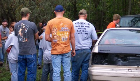 1978 Ford Bronco - Several people stand around a car, some looking at the trunk. One man's shirt has a humorous slogan about mud hunting.