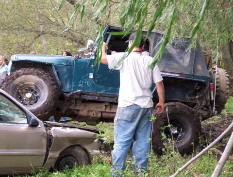 1978 Ford Bronco - A teal Jeep Wrangler is stuck in the mud, its front end resting on a wrecked tan car.