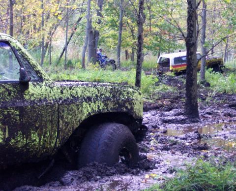 1978 Ford Bronco - Several vehicles are stuck in the mud in a forest setting, with one partially submerged.