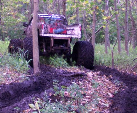1978 Ford Bronco - A heavily muddied truck navigates a difficult path through a dense forest.