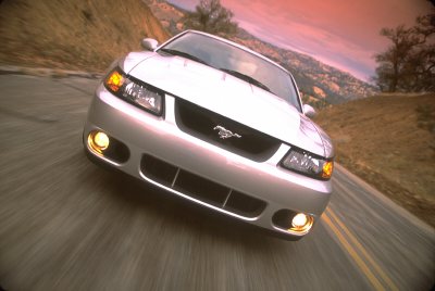 2003 Ford Mustang - Silver 2003 Ford Mustang driving on a road with hills in the background.