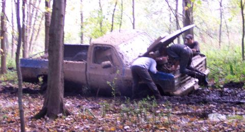 1978 Ford Bronco - People attempt to fix a mud-stuck pickup truck in a wooded area.
