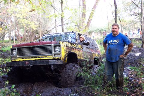 1978 Ford Bronco - A man poses next to a heavily mud-covered off-road vehicle stuck in a muddy wooded area.