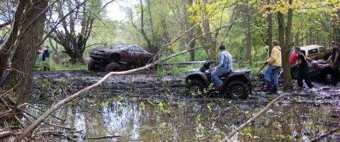 1978 Ford Bronco - Several vehicles are stuck in deep mud in a wooded area, with people attempting to free them.