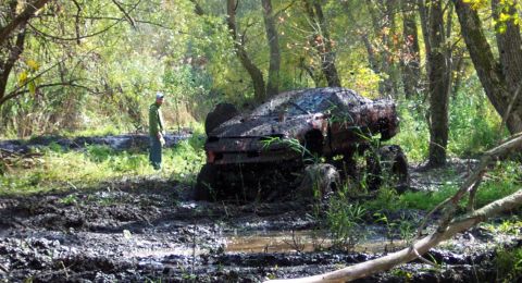1978 Ford Bronco - Off-road vehicle deeply stuck in mud and vegetation, with a person observing the situation.