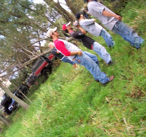 1978 Ford Bronco - Several people are gathered around a red SUV that appears to be stuck among trees.