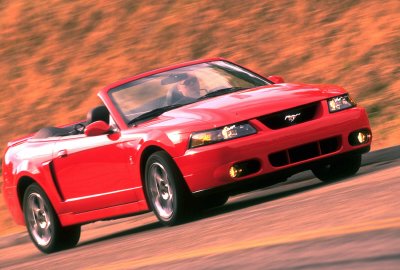 2003 Ford Mustang - A red 2003 Ford Mustang convertible is captured in motion on a blurred background.