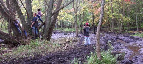 1978 Ford Bronco - A group of people are in a muddy, wooded area with trees and foliage.