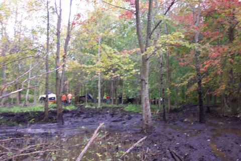 1978 Ford Bronco - Several off-road vehicles are stuck in a muddy forest clearing during autumn.