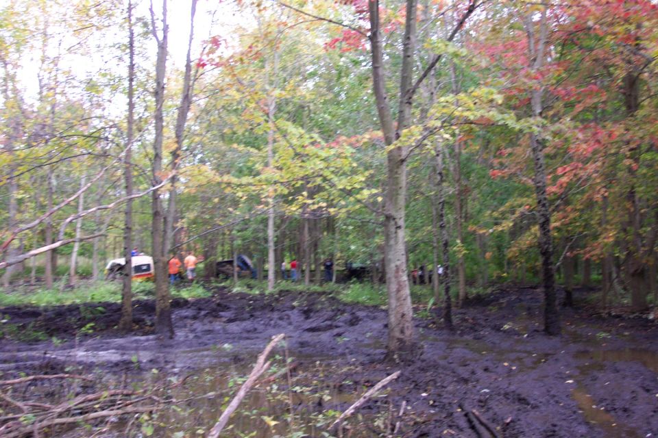 White and orange off-road vehicle stuck in mud with people around