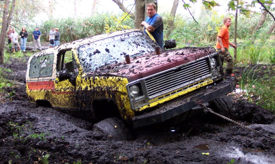Mud-covered off-road vehicle stuck in deep mud, with people watching