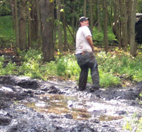 1978 Ford Bronco - Man stands in a muddy, wooded area with puddles and trees.